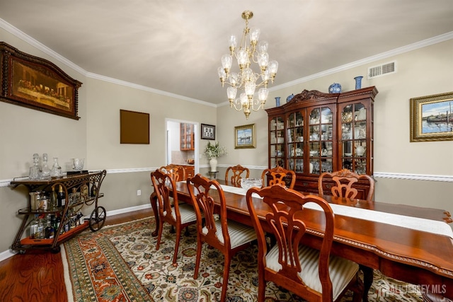 dining room featuring crown molding, visible vents, wood finished floors, a chandelier, and baseboards