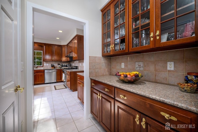 kitchen featuring light tile patterned floors, glass insert cabinets, appliances with stainless steel finishes, under cabinet range hood, and backsplash