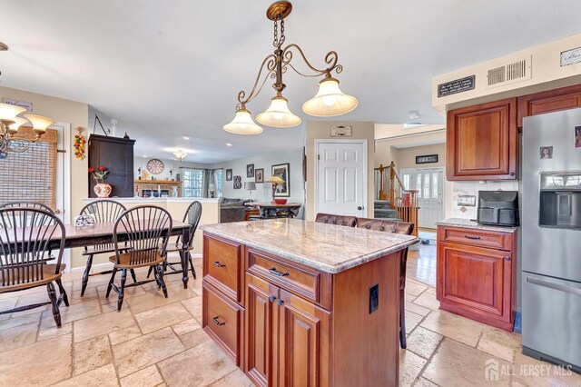 kitchen with stainless steel refrigerator with ice dispenser, a center island, light stone countertops, and pendant lighting