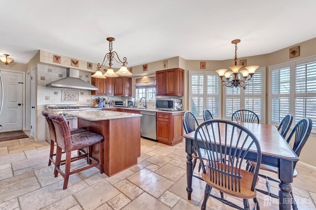 kitchen with stainless steel appliances, a center island, decorative light fixtures, and wall chimney exhaust hood