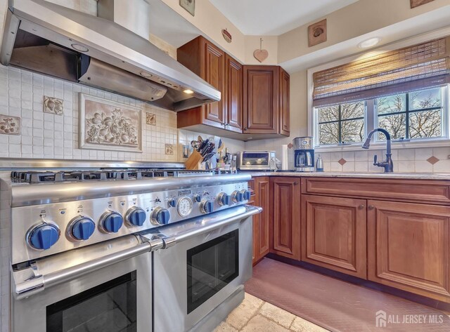 kitchen with tasteful backsplash, wall chimney exhaust hood, double oven range, and sink