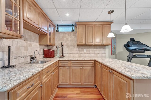 kitchen with decorative light fixtures, sink, decorative backsplash, kitchen peninsula, and light hardwood / wood-style flooring