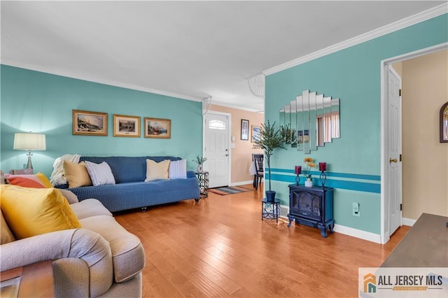 living room featuring crown molding, a wood stove, wood finished floors, and baseboards