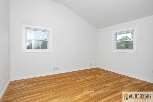 spare room with vaulted ceiling, light wood finished floors, and baseboards