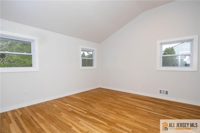 empty room featuring healthy amount of natural light, lofted ceiling, light wood-style flooring, and baseboards