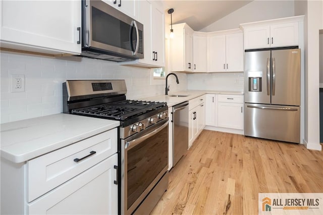 kitchen featuring stainless steel appliances, a sink, white cabinetry, light wood-style floors, and light stone counters