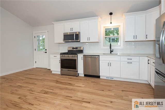 kitchen with stainless steel appliances, a sink, decorative backsplash, light wood-type flooring, and light countertops