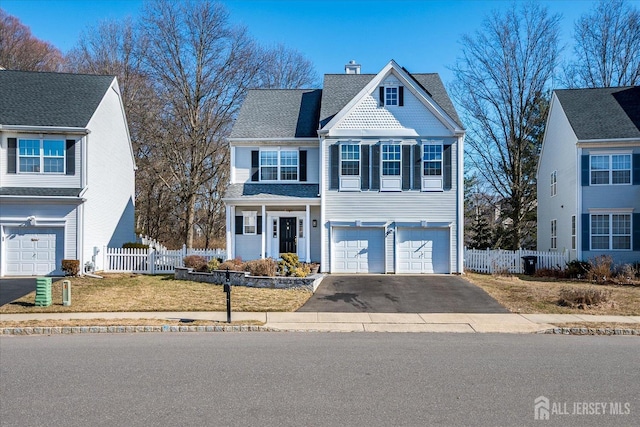 traditional-style house featuring aphalt driveway, an attached garage, a shingled roof, fence, and a chimney