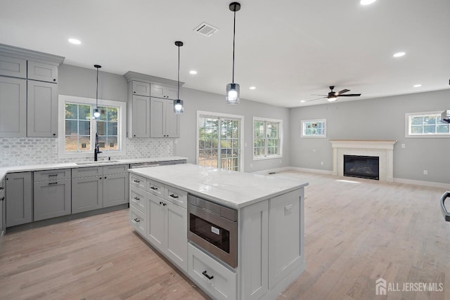 kitchen featuring backsplash, ceiling fan, built in microwave, sink, and hanging light fixtures