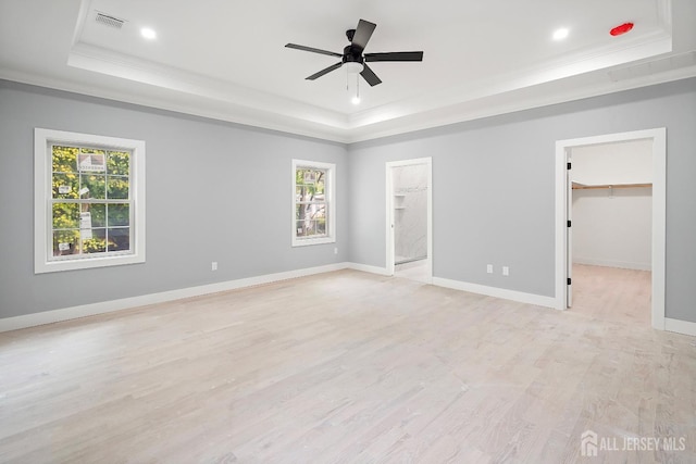 unfurnished room featuring ceiling fan, a healthy amount of sunlight, a raised ceiling, and light hardwood / wood-style flooring