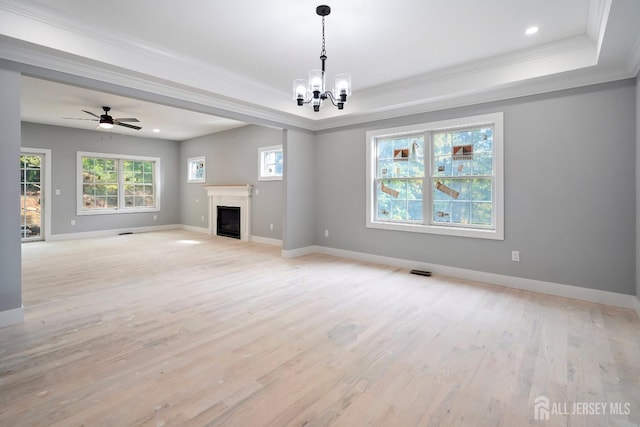 unfurnished living room featuring ceiling fan with notable chandelier, light hardwood / wood-style floors, crown molding, and a tray ceiling