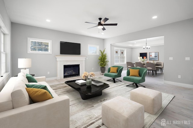 living room with a premium fireplace, ceiling fan with notable chandelier, and light wood-type flooring