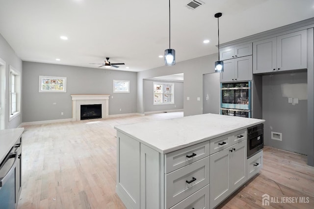 kitchen featuring gray cabinetry, built in microwave, a center island, ceiling fan, and hanging light fixtures