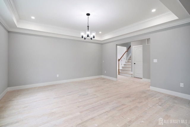 empty room featuring a chandelier, light hardwood / wood-style floors, and a tray ceiling