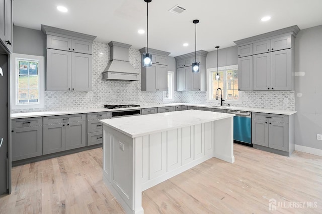 kitchen featuring stainless steel appliances, decorative light fixtures, gray cabinets, a kitchen island, and custom exhaust hood