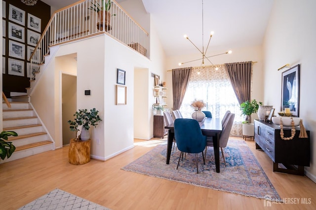 dining area with a towering ceiling, light hardwood / wood-style floors, and a notable chandelier