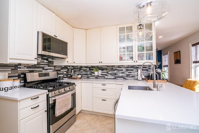 kitchen with light tile patterned flooring, appliances with stainless steel finishes, decorative light fixtures, sink, and white cabinets