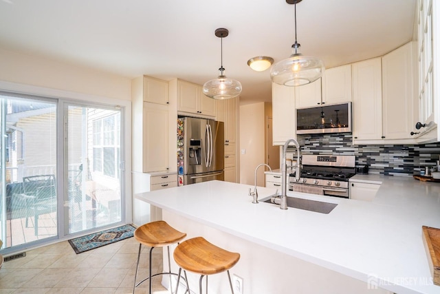 kitchen with appliances with stainless steel finishes, decorative light fixtures, sink, backsplash, and kitchen peninsula