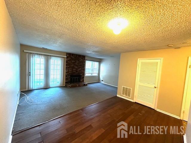 unfurnished living room with a fireplace, a textured ceiling, and dark hardwood / wood-style floors