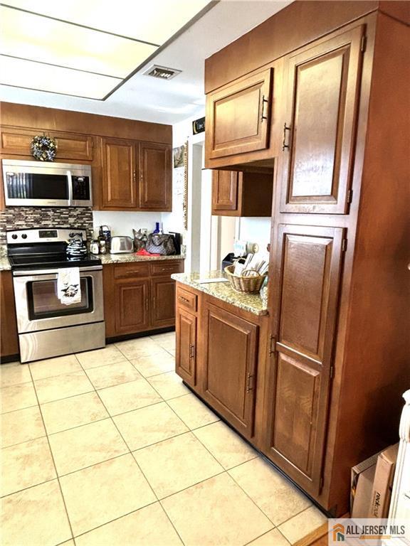 kitchen with tasteful backsplash, light stone countertops, light tile patterned flooring, and stainless steel appliances