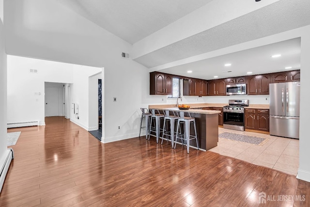 218 Community Cir, Old Bridge, NJ 08857 - kitchen with stainless steel appliances, baseboard heating, dark brown cabinetry, high vaulted ceiling, and a breakfast bar area