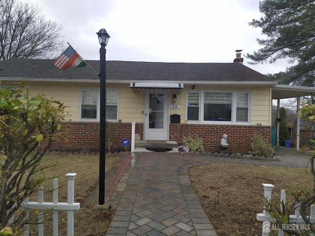 view of front of house featuring an attached carport, brick siding, and a chimney