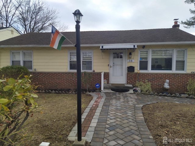 view of front facade with roof with shingles, a chimney, and brick siding