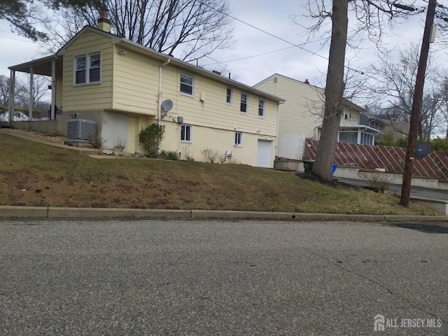 view of home's exterior with central AC, a yard, a chimney, and an attached garage