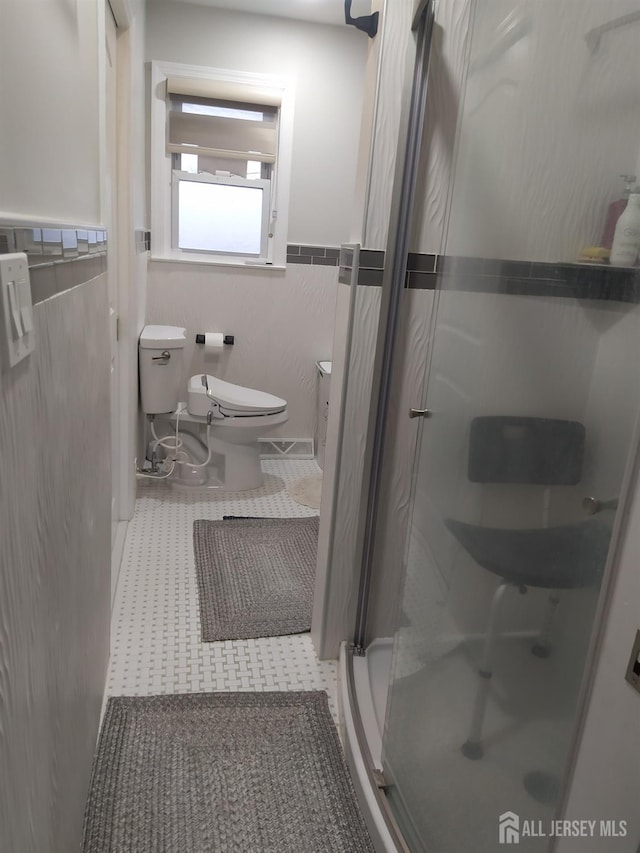 full bathroom with toilet, a shower stall, tile walls, and wainscoting