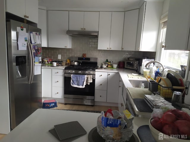 kitchen with decorative backsplash, appliances with stainless steel finishes, light countertops, under cabinet range hood, and a sink