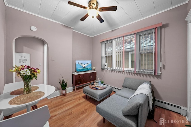 living area with a ceiling fan, baseboards, light wood-style floors, baseboard heating, and crown molding