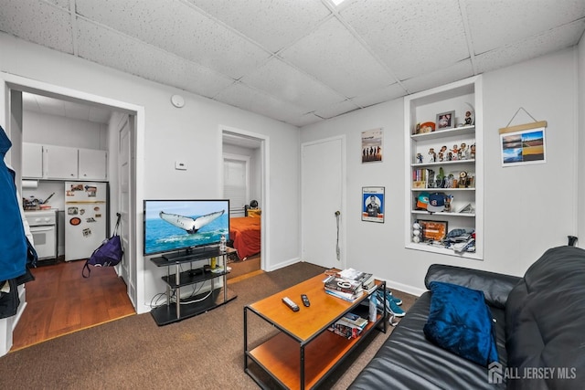 living room with built in features, a drop ceiling, and baseboards