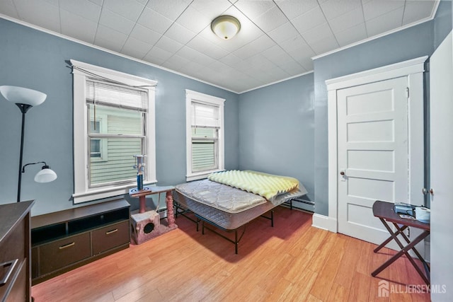 bedroom with baseboards, light wood finished floors, baseboard heating, and crown molding