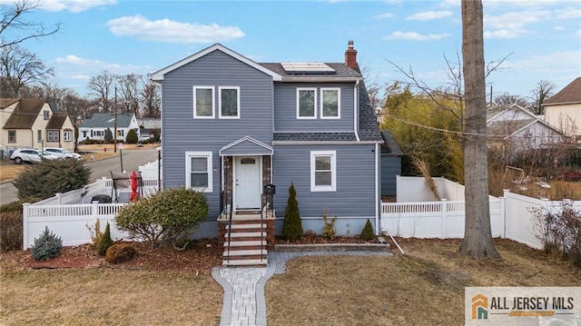 view of front of home featuring a fenced backyard, a chimney, solar panels, and roof with shingles