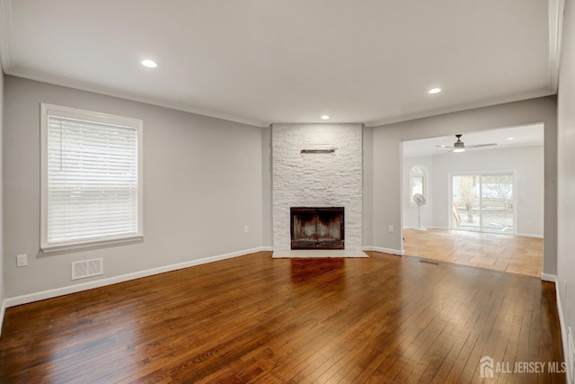 unfurnished living room with baseboards, a stone fireplace, visible vents, and hardwood / wood-style flooring