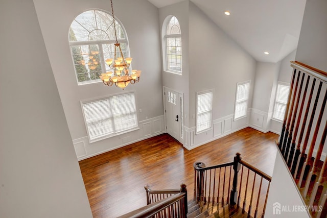foyer with a notable chandelier, a decorative wall, high vaulted ceiling, and wood finished floors
