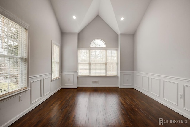 unfurnished room with vaulted ceiling, hardwood / wood-style flooring, and a wainscoted wall