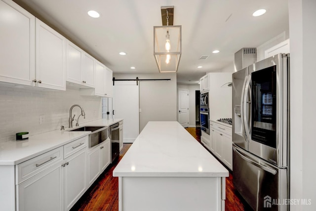 kitchen with a center island, a sink, a barn door, appliances with stainless steel finishes, and dark wood-style floors
