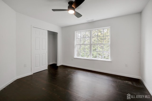 unfurnished bedroom featuring wood finished floors, a closet, visible vents, baseboards, and ceiling fan
