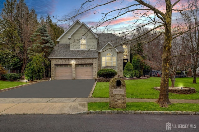 traditional-style house featuring a lawn, brick siding, an attached garage, a shingled roof, and aphalt driveway