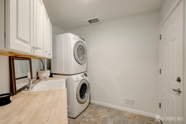 washroom with a sink, cabinet space, stacked washer and dryer, visible vents, and baseboards