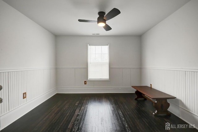 spare room featuring a wainscoted wall, visible vents, a ceiling fan, and hardwood / wood-style flooring