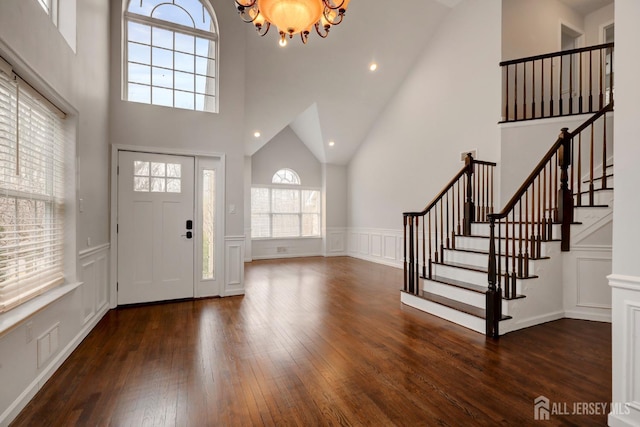 foyer with an inviting chandelier, wood-type flooring, stairs, a decorative wall, and high vaulted ceiling