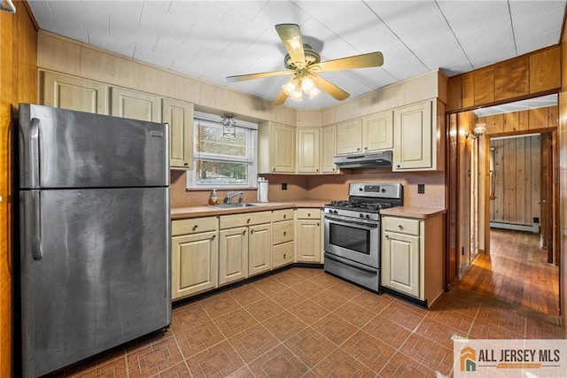 kitchen featuring a baseboard heating unit, sink, ceiling fan, appliances with stainless steel finishes, and wooden walls