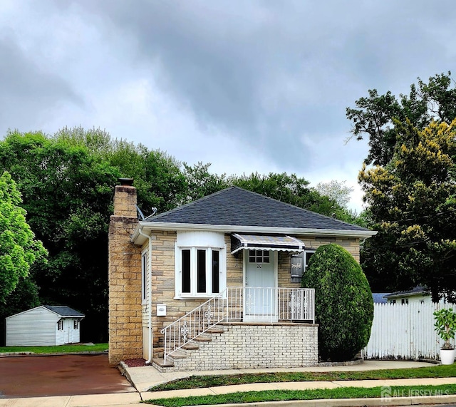 20 Brunswick Ave, Spotswood, NJ 08884 - bungalow featuring a chimney, roof with shingles, stone siding, and a storage unit