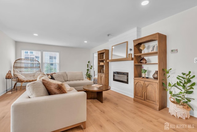 living room featuring baseboards, recessed lighting, light wood finished floors, and a glass covered fireplace