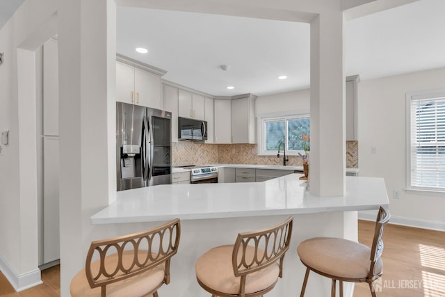 kitchen featuring a breakfast bar area, backsplash, appliances with stainless steel finishes, and light wood-style flooring
