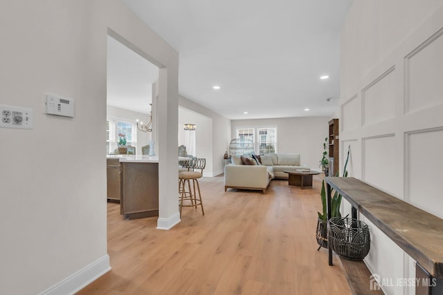 living room with baseboards, light wood-type flooring, a notable chandelier, and recessed lighting