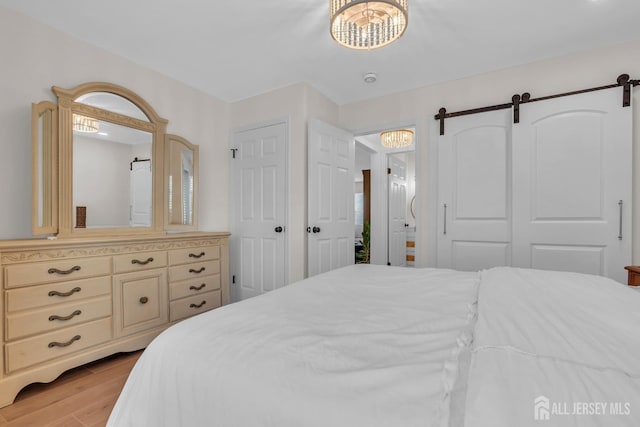 bedroom with a notable chandelier, a barn door, and light wood-style floors