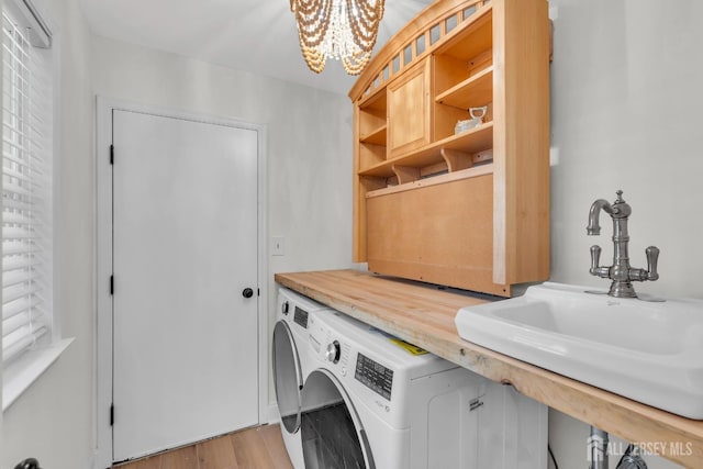laundry room with a sink, light wood-type flooring, washer / dryer, a notable chandelier, and laundry area